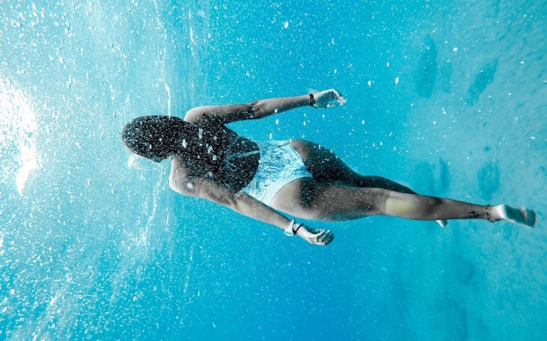 Frau in weißen Badeanzug taucht im Meer umgeben von unzähligen Wasserblasen
